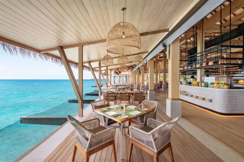 Restaurante frente al mar en el Hilton Maldives, con mesas al aire libre y vistas directas a la laguna turquesa