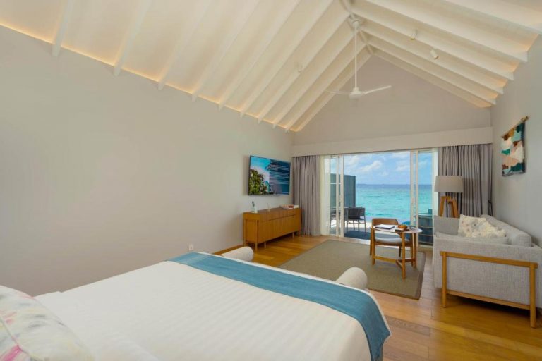 Interior de una Water Villa en RAAYA by Atmosphere, Maldivas, con dormitorio elegante y vista despejada al océano en Raa Atoll.